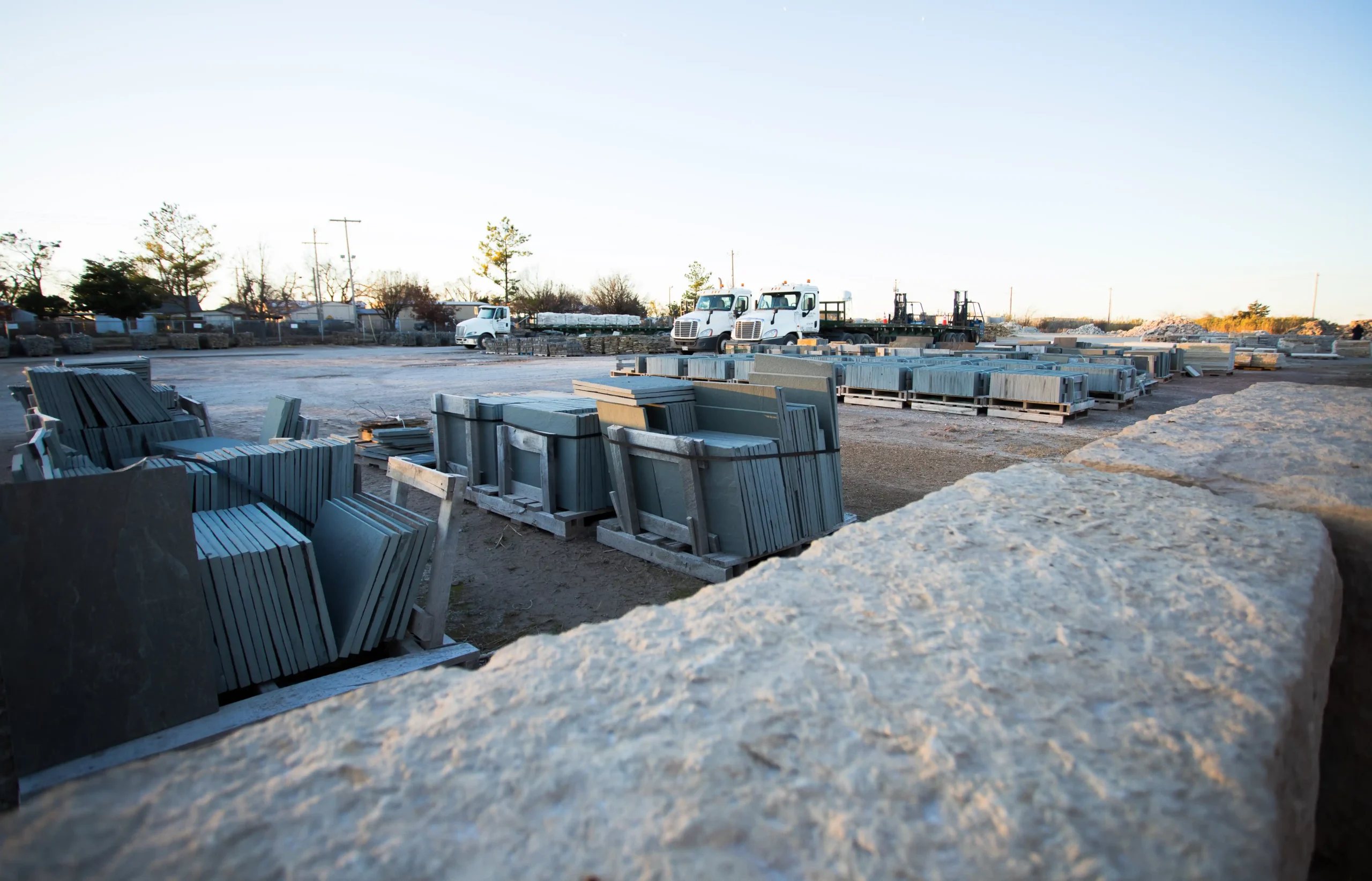 Stone slabs and flagstone stacked in an outdoor builders stone yard with trucks in the background