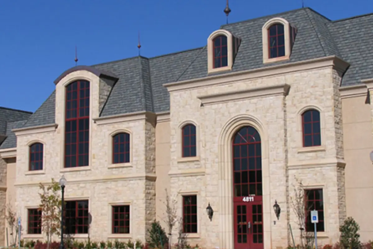 External view of the Gaillardia office building in Oklahoma City, featuring a blonde limestone facade, red divided lite windows, and a grey shingle roof
